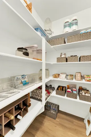 Walk-in pantry featuring extensive white shelving, built-in wine storage, wood-finish flooring, and ample storage capacity