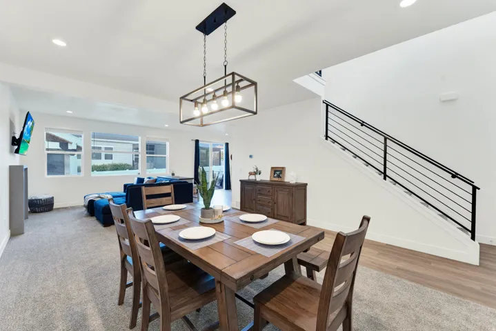 Open-concept living area featuring a modern linear chandelier, wood-finish flooring, and white walls