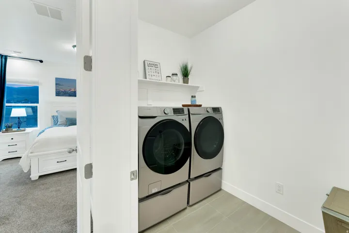 Dedicated laundry area featuring a white floating shelf and light-toned floor tiling