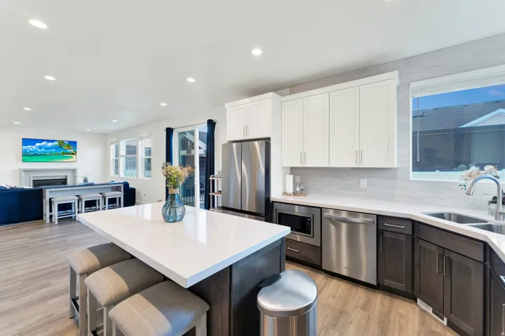 Open-concept kitchen featuring a white quartz-topped island, stainless steel appliances, two-tone cabinetry, and wood-finish flooring