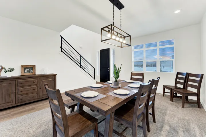 Dining area featuring a modern linear chandelier, large multi-pane window, wood-finish flooring, and a contemporary staircase with black metal railings