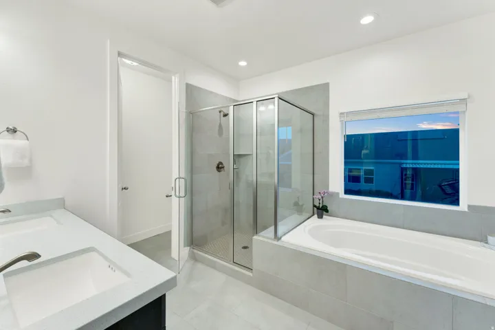 Contemporary bathroom featuring a deep soaking tub with tile surround, a glass-enclosed shower with tile walls, a dual vanity with integrated sinks, and recessed lighting