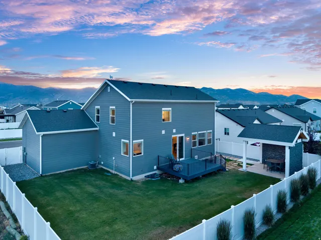 Spacious fenced backyard featuring a groomed lawn, private deck, and covered patio with stone facade