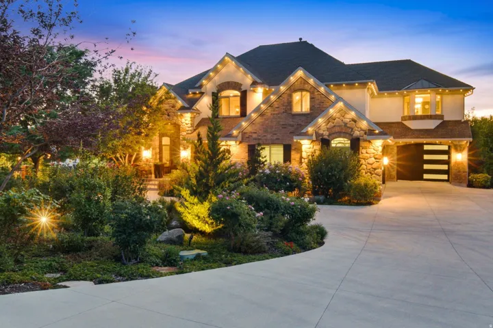 Stately residence featuring a stone and brick facade, a multi-car driveway, mature landscaping, and an integrated garage with modern horizontal paneling