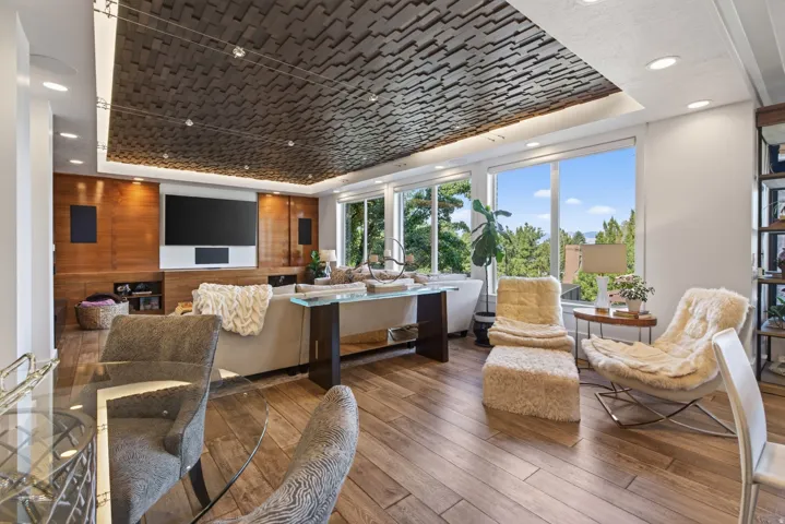 Living space featuring wood-finish flooring, a wood-paneled accent wall with built-in media console, recessed lighting, and large windows