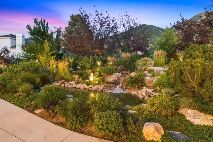 Landscaped rock garden featuring a pond, waterfall, diverse plantings, and integrated lighting