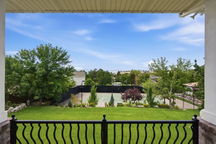 Guest House Expansive backyard featuring a tennis court, manicured lawn, mature trees, and a black wrought iron railing