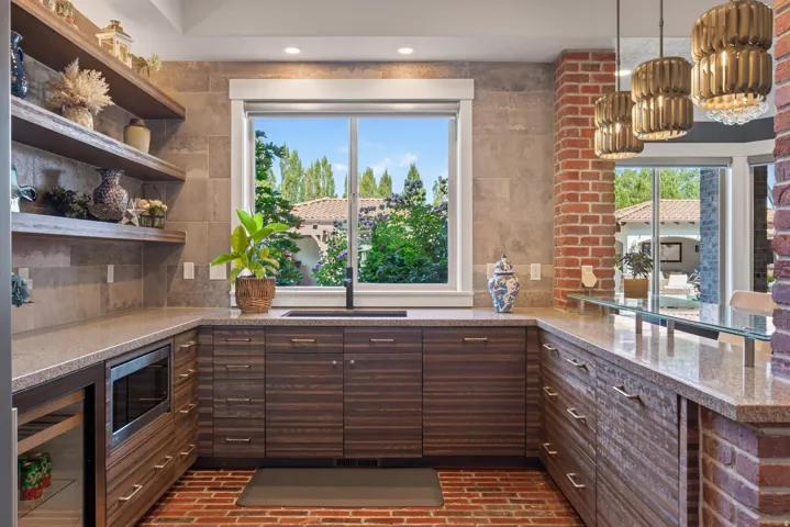 Built-in kitchen area featuring wood-finish cabinetry, stone countertops, and a brick-patterned floor