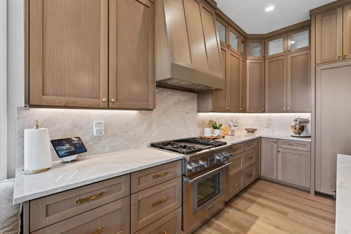 Guest House Gourmet kitchen featuring neutral-toned cabinetry, a stainless steel range with a custom hood, marble-finish countertops, and a full-height backsplash