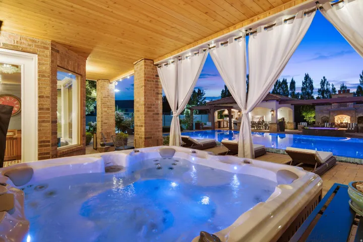 Covered patio featuring an illuminated spa, brick columns, a wood-finish ceiling, and sheer curtains
