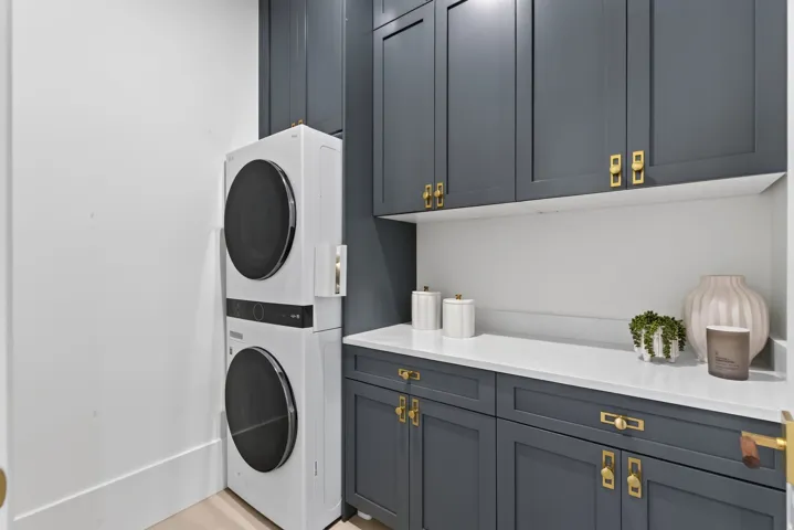 Guest House Laundry area featuring stacked appliances, dark cabinetry, light countertops, and a white backsplash
