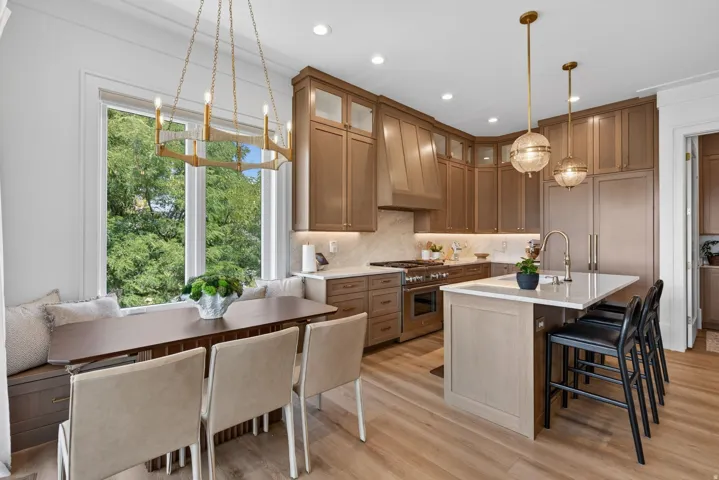 Guest House Modern kitchen featuring extensive wood-finish cabinetry, a large center island with seating, stainless steel appliances, and light wood-finish flooring