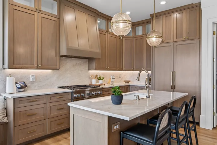 Guest House Kitchen featuring custom light wood-finish cabinetry, integrated paneled refrigeration, stainless steel professional-grade range, full-height stone backsplash, and a central island with undermount sink