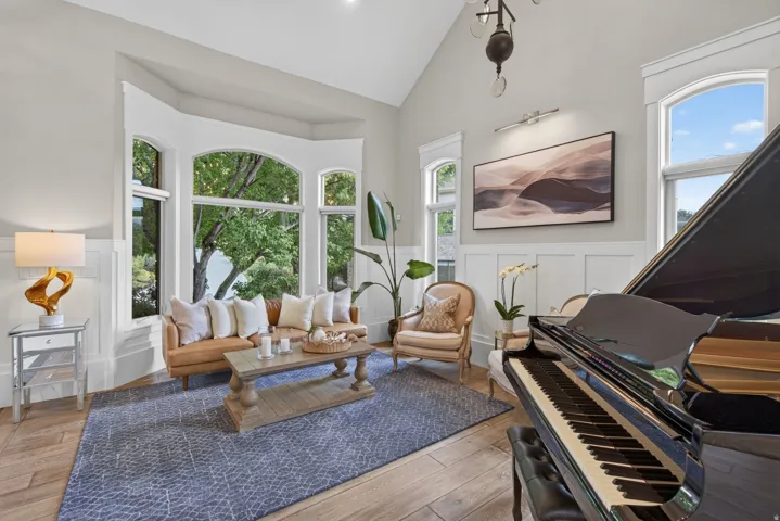 Spacious living area featuring a prominent bay window, wood-finish flooring, wainscoting details, and a vaulted ceiling