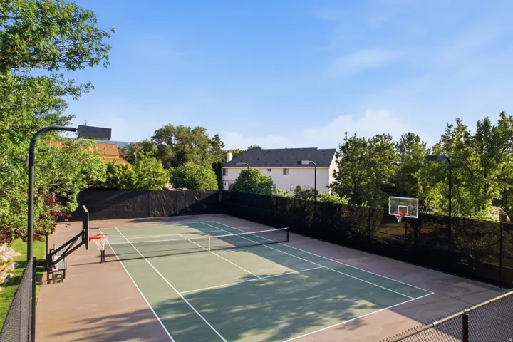 Multi-sport court featuring a tennis net, basketball hoops with backboards, and perimeter fencing