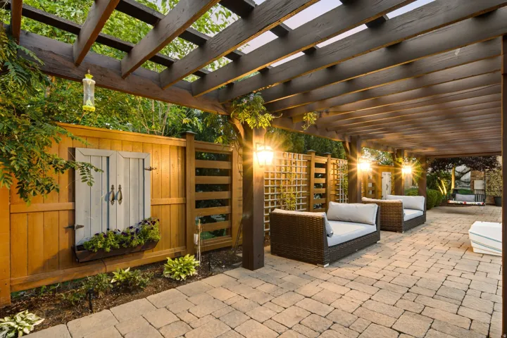 Expansive stone paver patio featuring a wooden pergola, built-in outdoor lighting, and a privacy fence with decorative trellis panels