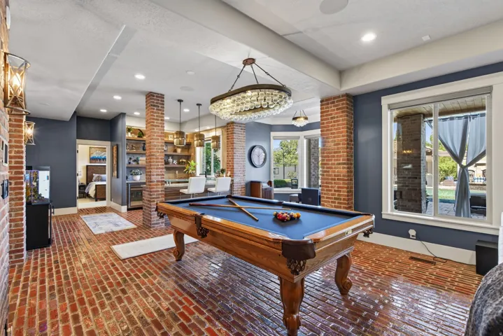 Entertainment room featuring brick flooring, a built-in wet bar with shelving, a large window, recessed lighting, and exposed brick columns