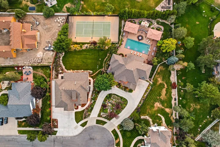 Expansive property featuring a tennis court, a swimming pool with a surrounding patio, mature landscaping, and a curvilinear driveway
