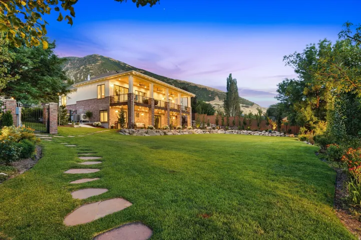 Expansive lawn with natural stone stepping path leading to a two-story residence featuring brick lower siding, upper level stucco, and multiple balconies with metal railings