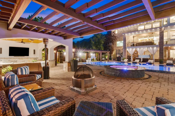 Expansive paver patio featuring a built-in outdoor kitchen with a large screen, a recessed fire pit, and a swimming pool