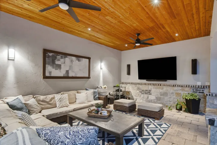 Covered outdoor living space featuring a natural wood plank ceiling, recessed lighting, and dual ceiling fans