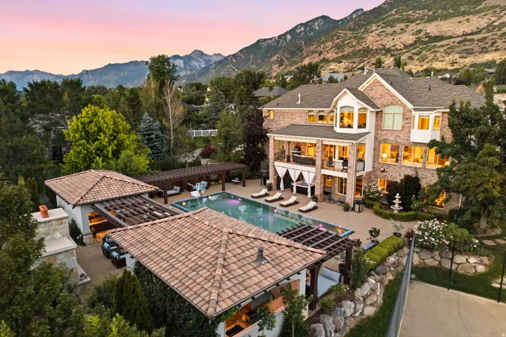 Expansive terraced backyard featuring a large swimming pool with integrated lighting, multiple lounge areas, and a dedicated pool house with a covered patio