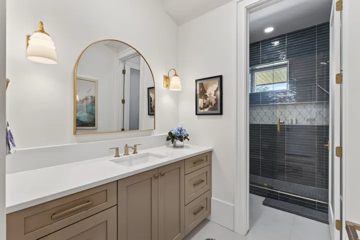 Guest House Bathroom vanity featuring a light-colored countertop, dual-tone cabinetry, and a gold-framed arched mirror