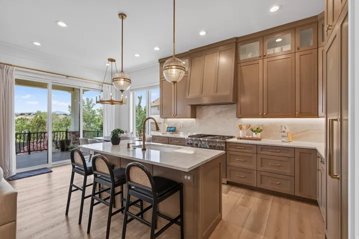 Guest House Gourmet kitchen featuring a large central island with seating, wood-finish flooring, custom cabinetry with glass accents, stone countertops with a matching backsplash, and high-end stainless steel appliances