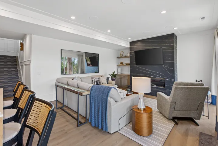 Guest House Spacious living area featuring a prominent dark stone fireplace with integrated linear firebox, wood-finish flooring, recessed lighting, and crown molding