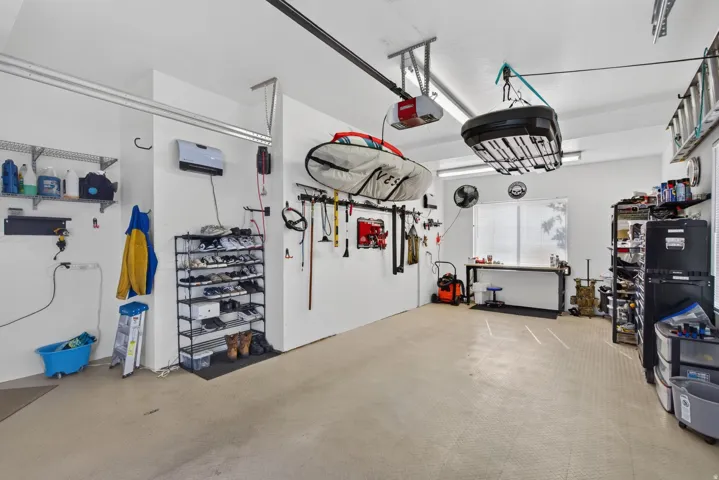 Guest House Spacious garage featuring light-toned flooring, white walls, overhead lighting, an overhead storage system, and a dedicated workspace