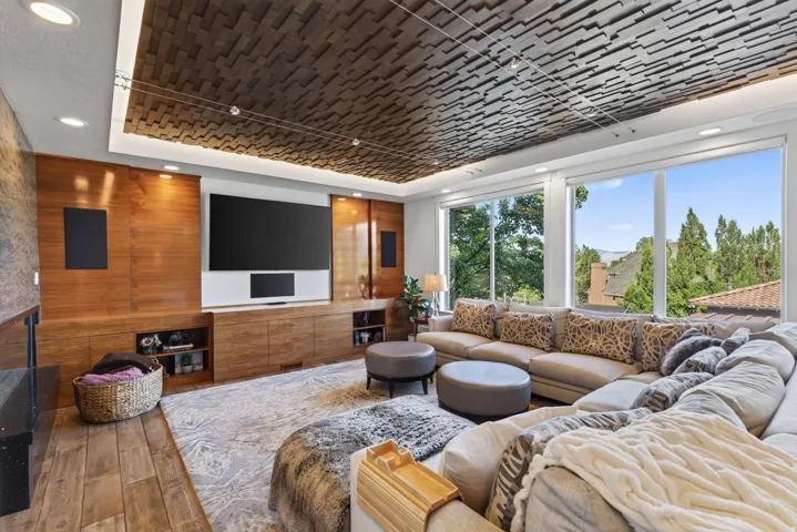 Living area with floor-to-ceiling windows, a wood-paneled entertainment wall with integrated cabinetry, and a textured ceiling design