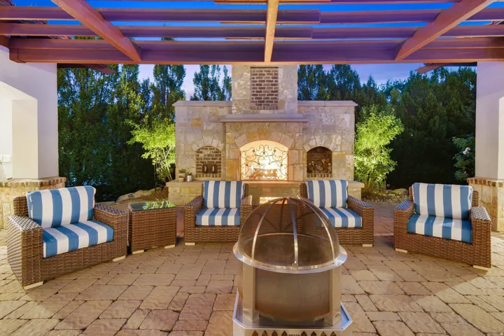 Expansive covered patio featuring a stone fireplace with brick accents, wood pergola, and paver flooring