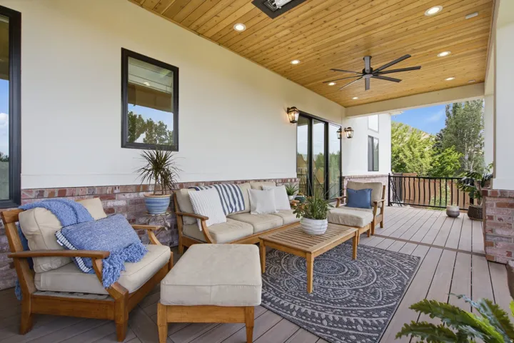 Guest House Spacious covered outdoor deck featuring a wood-finish ceiling with recessed lighting and ceiling fan, composite decking, brick and white siding accents, and sliding glass doors