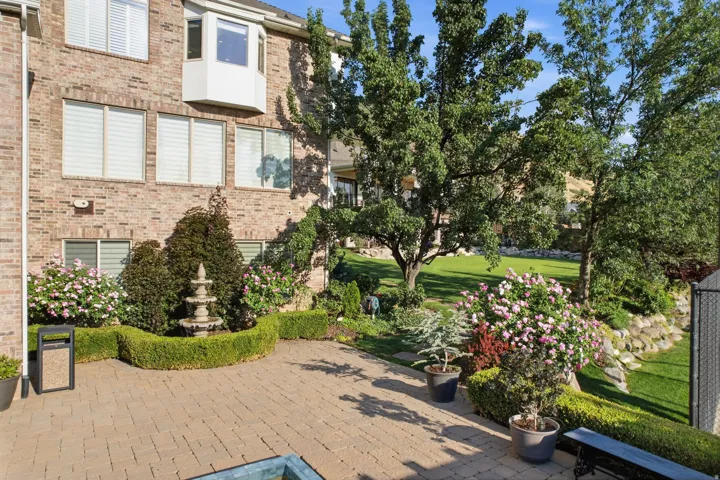 Guest House Expansive paver patio with a tiered fountain, surrounded by manicured shrubbery and mature trees