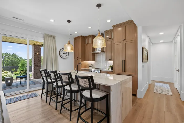 Guest House Contemporary kitchen featuring a large central island with seating for five, light wood-finish flooring, and recessed lighting