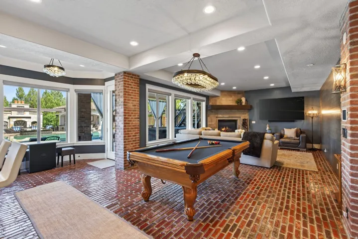 Spacious entertainment area featuring brick-finish flooring, a stone fireplace with a wood mantle, and extensive windows