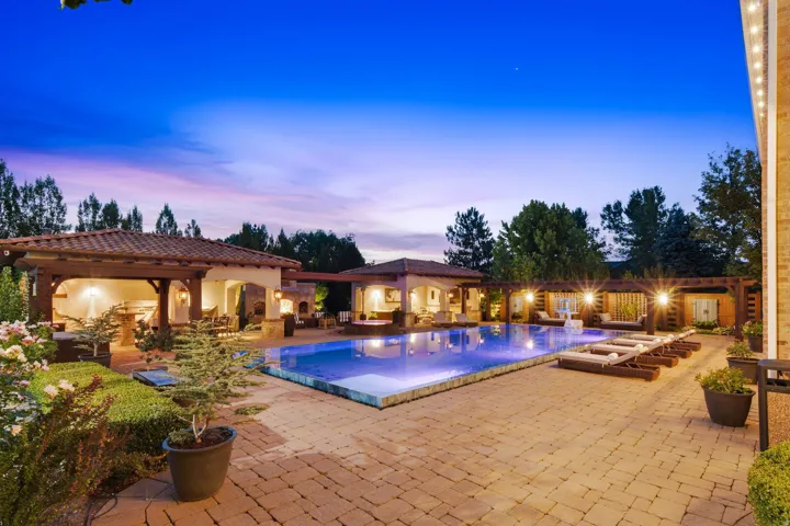 Expansive outdoor area featuring a rectangular swimming pool, paver patio, two covered cabanas with tile roofs, and a pergola structure