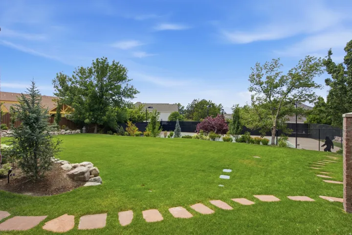 Guest House Expansive backyard featuring a lush lawn, mature trees, natural rock landscaping, stepping stone path, and a partially visible sports court