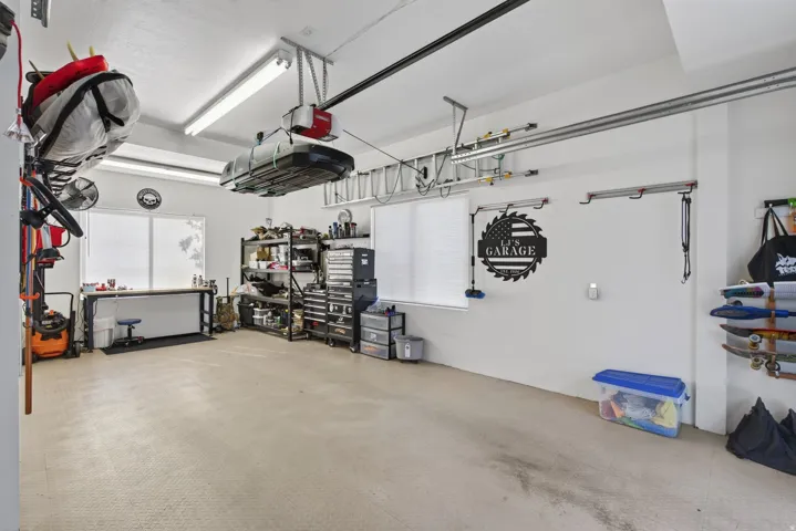 Guest House Spacious garage featuring light-toned interlocking floor tiles, bright overhead lighting, a built-in workbench, and wall-mounted storage tracks