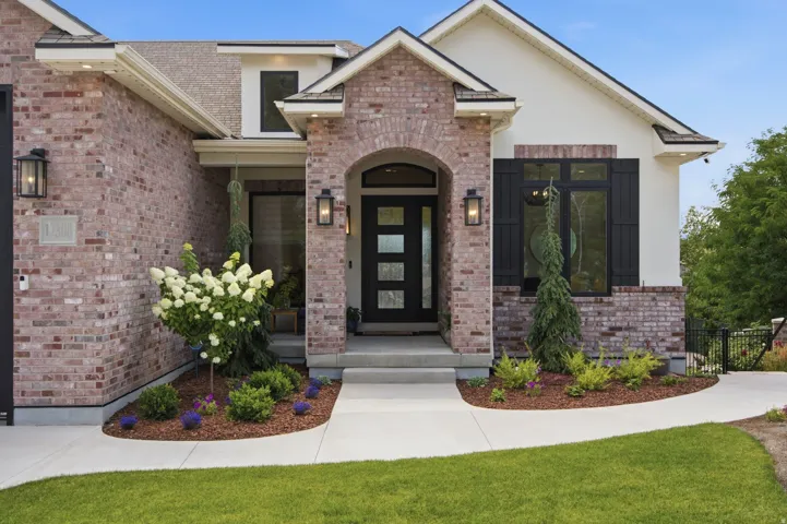 Guest House Brick and stucco exterior featuring a contemporary front entry door with obscure glass panels, an arched brick portico, black decorative shutters, and mature landscaping