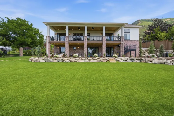 Guest House Expansive rear exterior featuring a large green lawn, a covered upper-level deck, and a covered lower-level patio