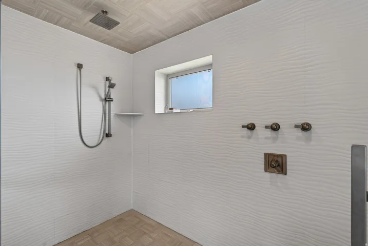 Walk-in shower featuring textured white wall tiling, a rain showerhead, Steam shower, and a handheld shower attachment