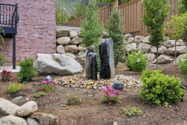 Guest House Landscaped terraced yard featuring a multi-column water feature with a pebble surround, retaining walls, mature plantings, and a red brick exterior