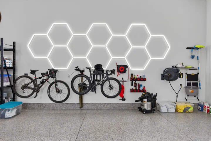 Guest House Garage space featuring an epoxy-coated floor, hexagonal wall lighting, wall-mounted storage racks, and overhead shelving