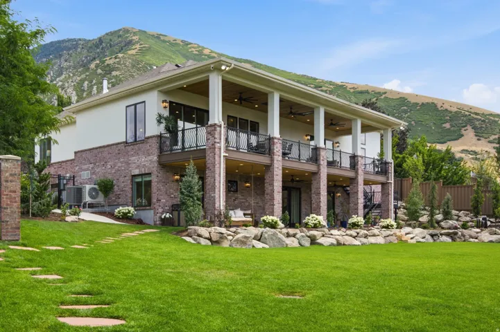 Guest House Two-story property featuring a brick and stucco exterior, dual covered patios with wrought iron railings, and a terraced backyard with stone retaining walls