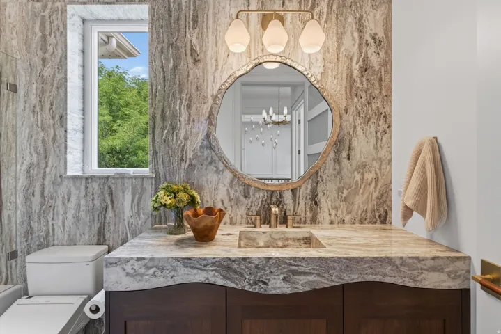 Guest House Floating vanity with a sculpted stone countertop and integrated basin, set against a full-height stone accent wall