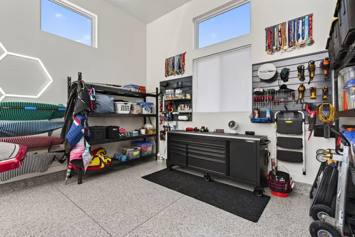 Garage space with high ceilings and transom windows, featuring epoxy flooring, slatwall organization, and built-in shelving