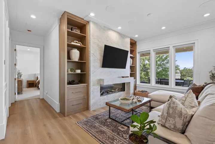 Guest House Living area featuring wide plank wood-finish flooring, a built-in linear fireplace with a stone surround, integrated wood shelving and cabinetry, and multiple large windows