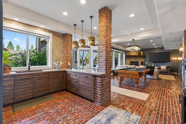 Open-concept space featuring brick flooring, a built-in wet bar with wood-finish cabinetry and stone countertops, and recessed lighting
