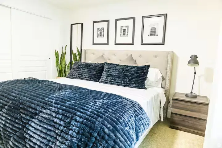 White wall panels featuring a tufted headboard, framed artwork, and light-toned carpeting